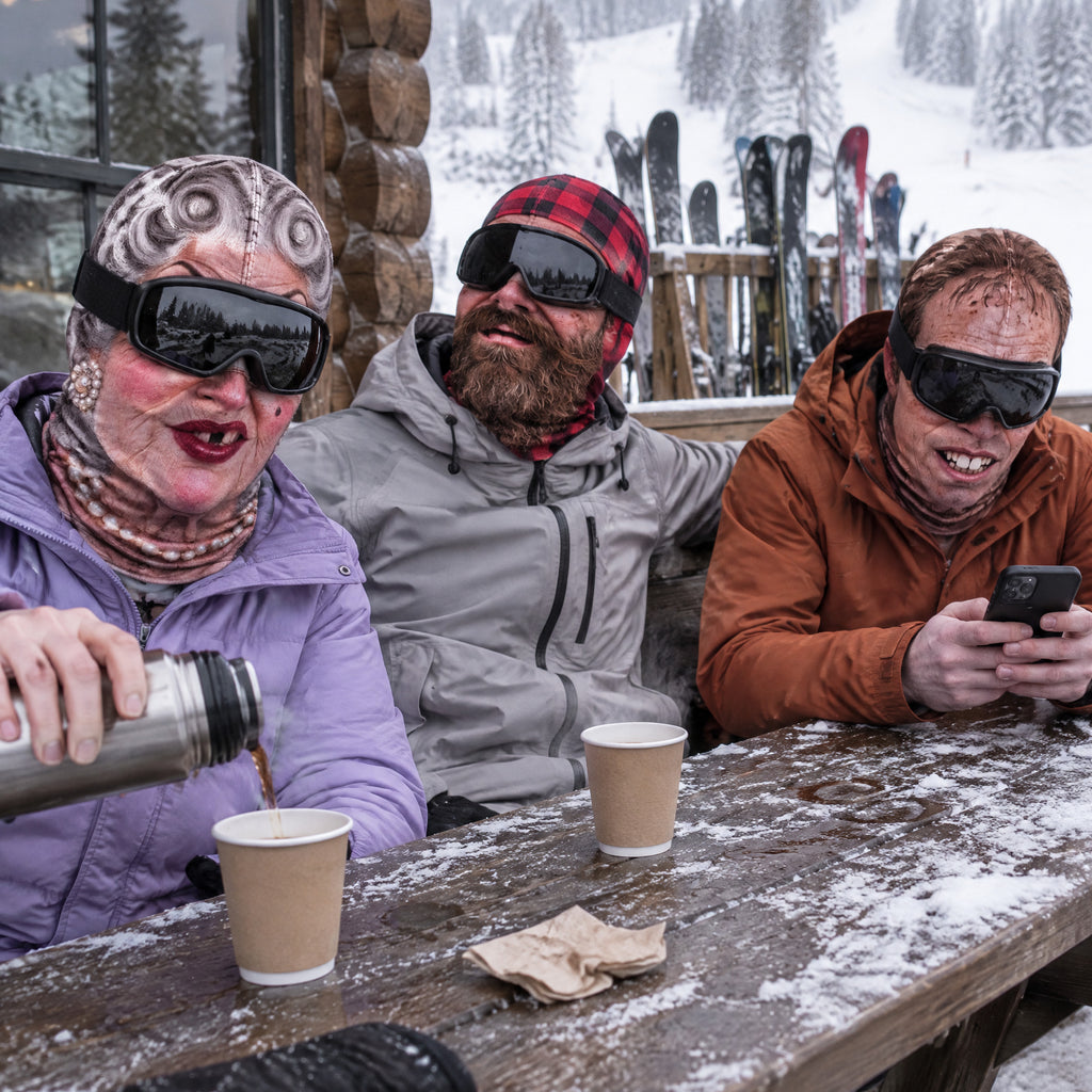 Three friends at a lodge table wearing printed face masks with goggles down
